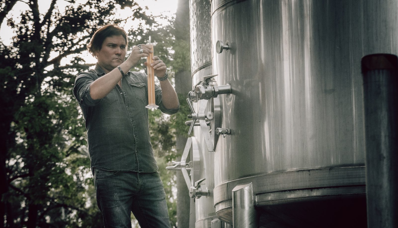 Head distiller reading a hydrometer against a fermenter at Mt Uncle