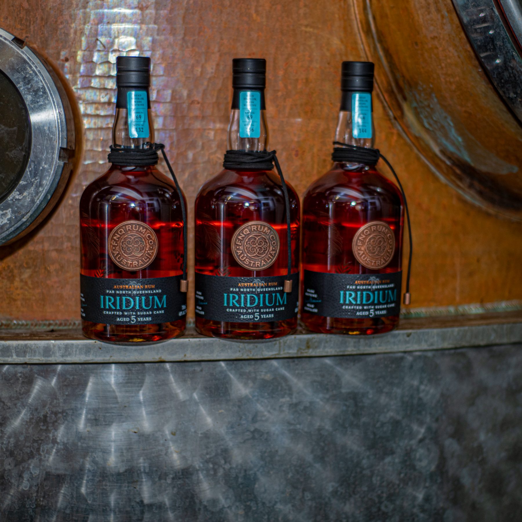 Three FNQ Rum Co. bottles standing on a cask beside the still at Walkamin