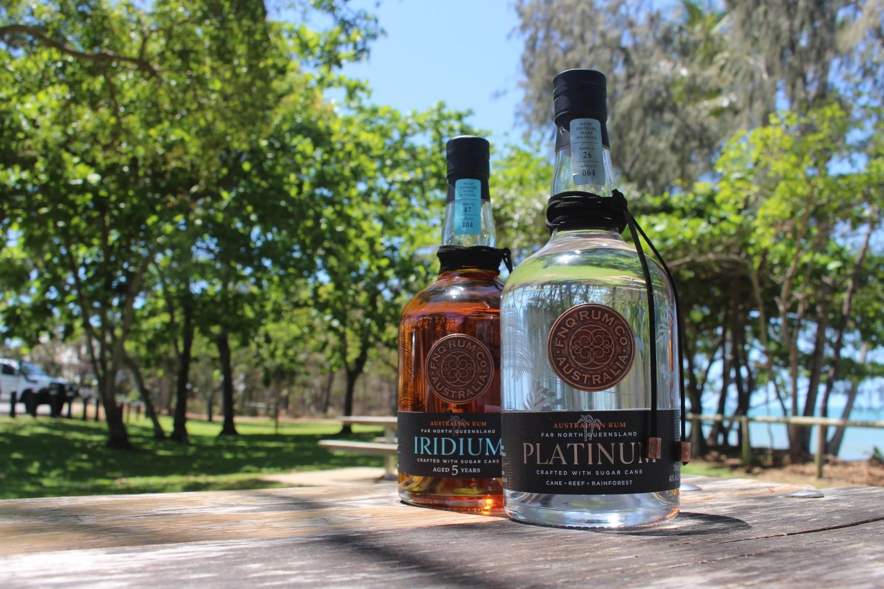 An FNQ Rum Co. Iridium and a Platinum bottle standing together on a table outdoors
