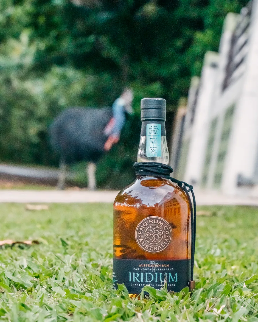 A bottle of FNQ Rum Co. Iridium standing on grass with a southern cassowary walking behind it